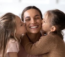 person with a dental bridge smiling as their children kiss either side of their cheeks