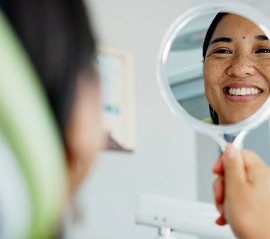Woman smiling at reflection in handheld mirror