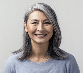 A middle-aged woman wearing a gray blouse and smiling because of her new and improved teeth