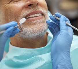 An older gentleman smiles after receiving his All-On-4 implants and allows a dental hygienist to examine his new teeth