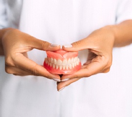 Manicured hands holding full set of traditional dentures in Fargo