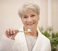 Senior woman in bathrobe brushing her teeth