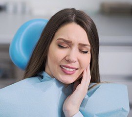 Grimacing woman in dental chair holding cheek