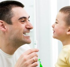 Father and young son brushing their teeth together