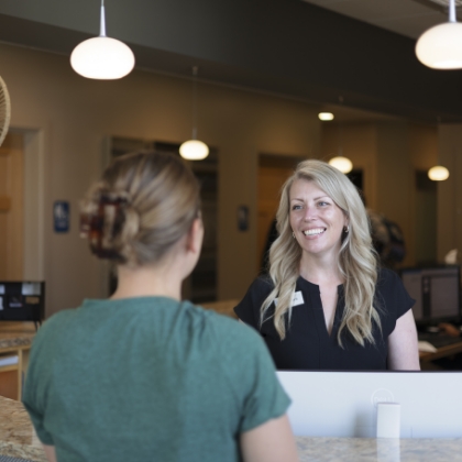 A woman with a bright smile is positioned at a reception desk, ready to assist visitors.