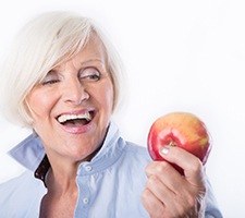 woman about to eat an apple as a health benefit of dental implants in Fargo