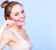 a woman brushing teeth for dental implant care in Fargo