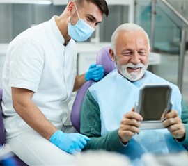 man looking in the mirror after getting dental implants in Fargo.