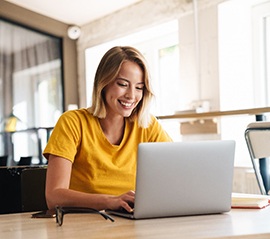 Smiling woman working on laptop after receiving dental implants in Fargo, ND