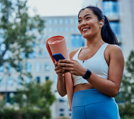 Smiling woman with yoga mat walking in park