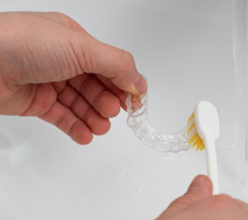Patient using toothbrush to clean aligner