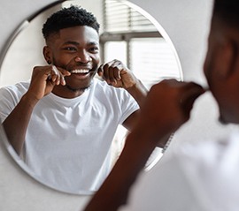 Man smiling while flossing his teeth in bathroom