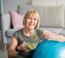 Smiling woman eating salad at home