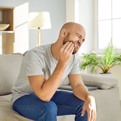Man struggling with toothache on couch at home