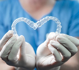Dental team member holding up two clear aligners in heart shape