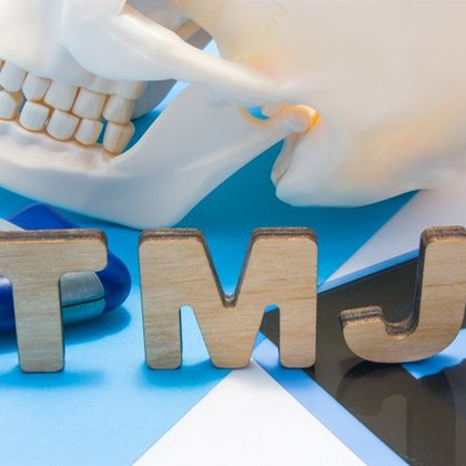 wooden letters spelling TMJ on a table next to teeth