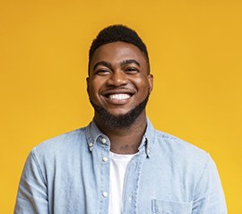 man with veneers in Fargo smiling in front of a yellow background 