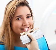 dentist holding a row of veneers up to a patient’s smile 