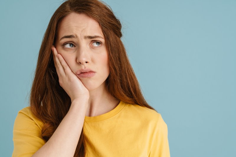 A woman holding her cheek because she needs emergency dentistry