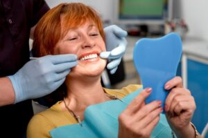 Woman admiring smile in hand-held mirror in dentist's chair.